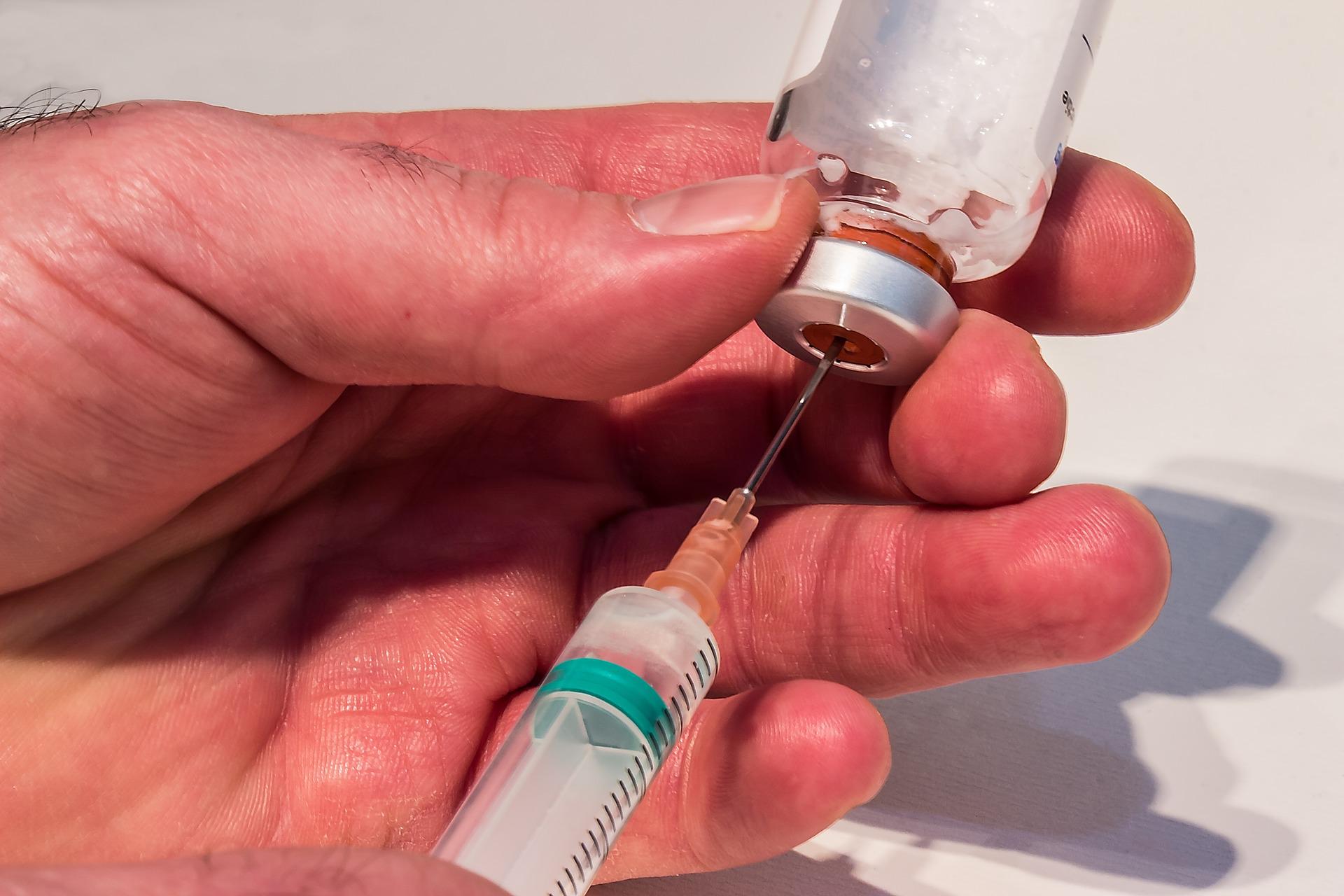 A Caucasian hand taking drugs with a syringe from a small injection bottle