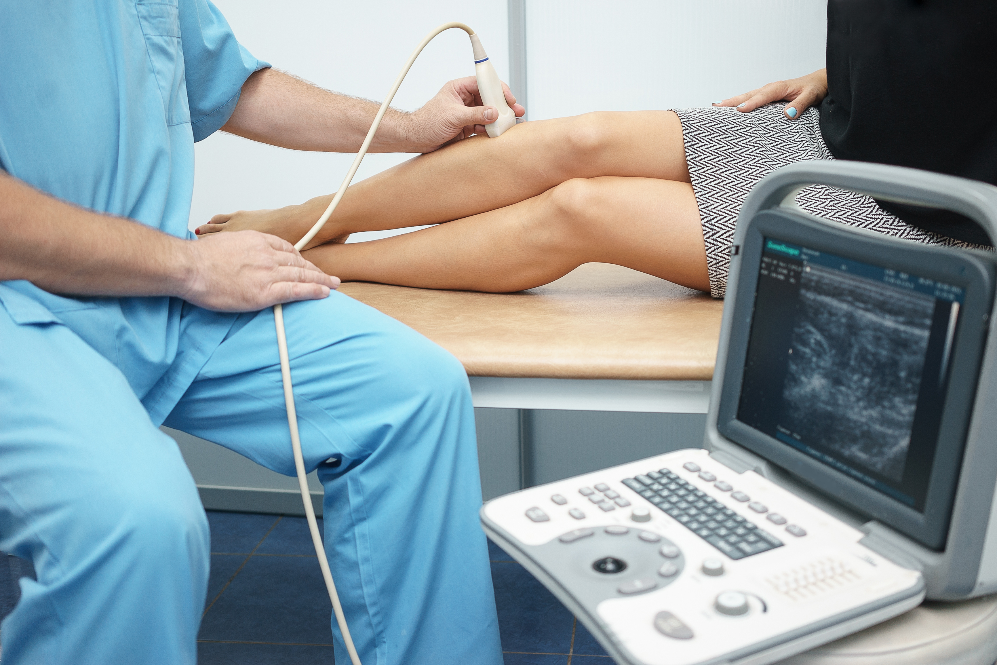 A doctor wearing a blue scrub performing an ultrasound on a woman