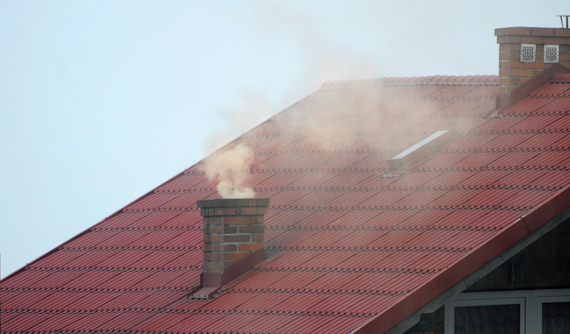A house with a red roof with its chimney emitting smoke
