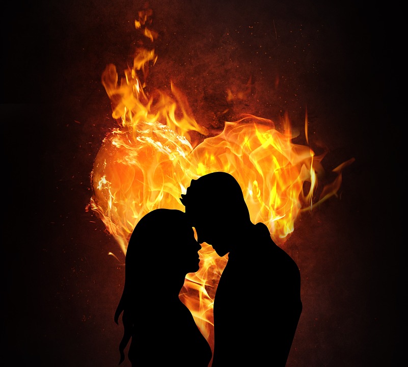 A boy is touching a girl's nose with his nose while fire is in their background