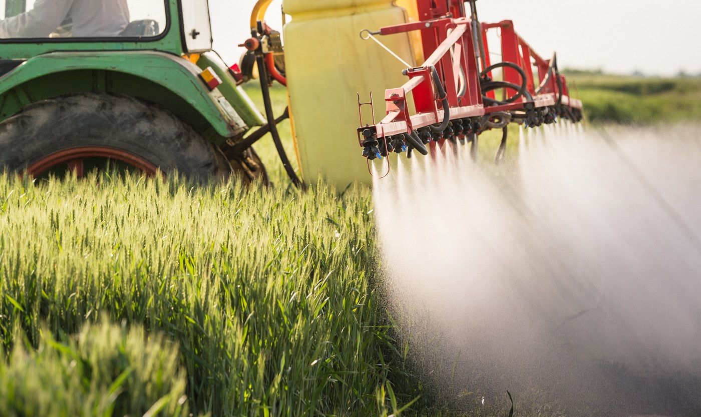 A green tractor spraying a farm field with chemical pesticides