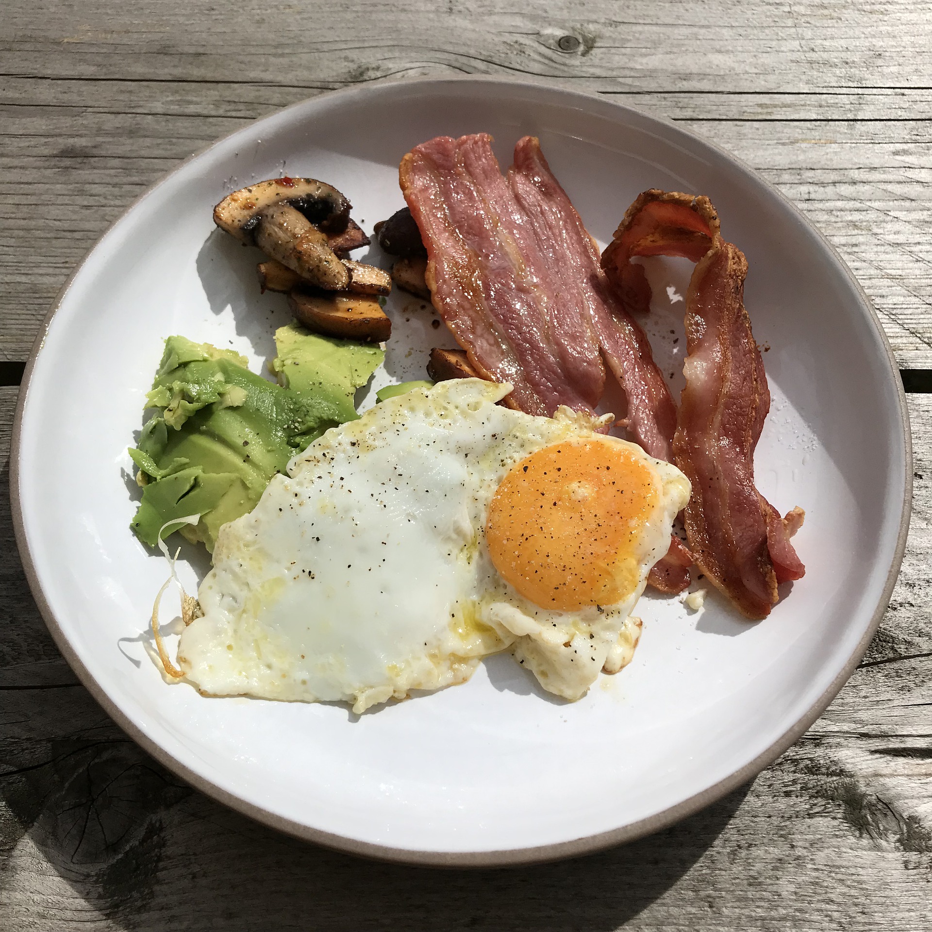 A white plate filled with some bacons, eggs, avocado, and meat